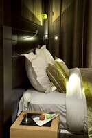A hotel room with a bed, pillows, a bedside table with a glass of milk and a pastry, and a curtain.