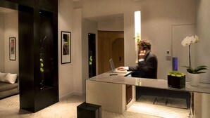 Een moderne hotellobby met een glazen receptiebalie, een bank en ingelijste kunstwerken.