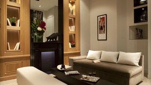 Een moderne woonkamer met een bank, salontafel en planken met boeken en decoratieve objecten.