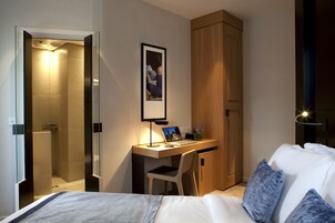 Habitación de hotel con cama, escritorio, laptop, silla, armario y ducha.