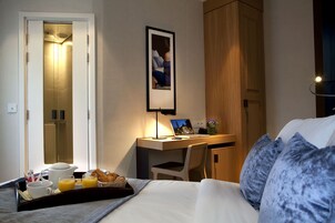 A hotel room with a bed, a desk with a laptop, a tray with breakfast items, and a framed photo on the wall.