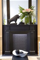 A fireplace with a black brick surround, a decorative sculpture, and a vase with flowers on the mantel.