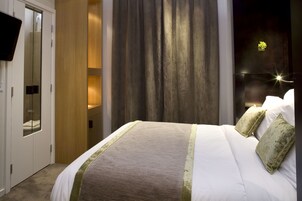 Una habitación de hotel con cama, televisor montado en la pared y armario de madera.