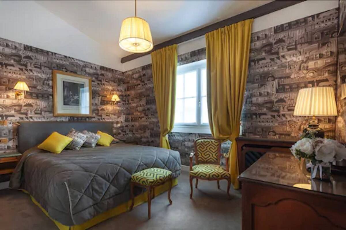A room with a bed, two chairs, a desk, and a window with curtains.