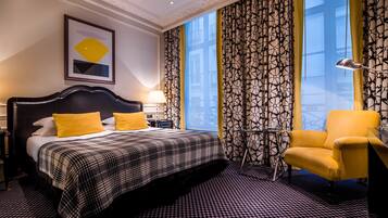 Une chambre d’hôtel avec un grand lit, une chaise, un bureau et une vue sur la ville grâce à de grandes fenêtres.