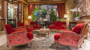 A traditional room with red upholstered furniture, a central table, and a large window with curtains.