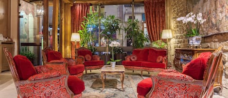 A traditional room with red upholstered furniture, a central table, and a large window with curtains.