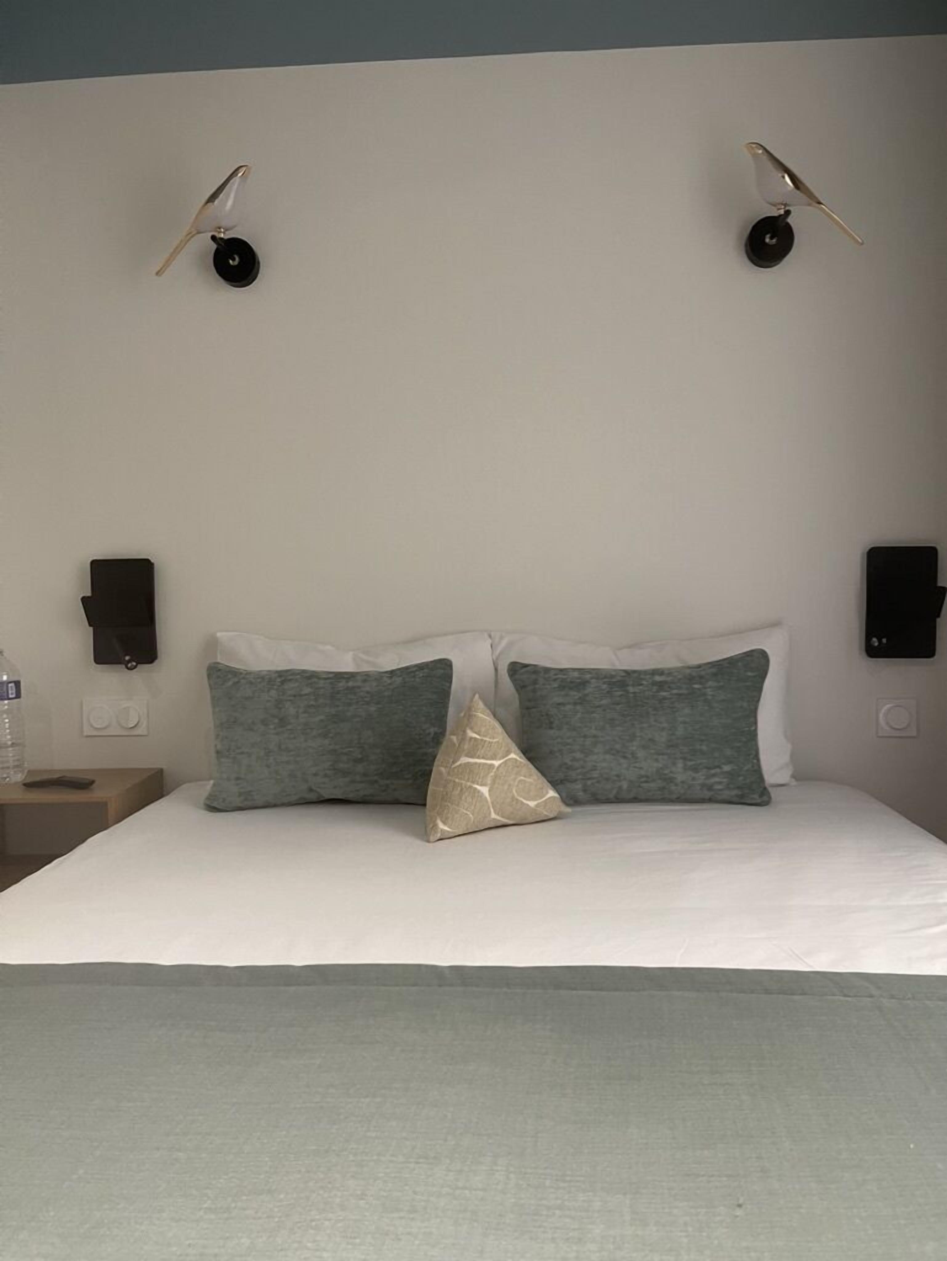 A neatly made bed with two pillows, a water bottle on a nightstand, and two wall-mounted speakers.