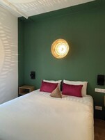 Een hotelkamer met een bed, kussens, een wandlamp en een nachtkastje.