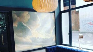 A room with a large window, a blue sofa, a wooden chair, and a round wooden stool. -  Hotelo Lyon Ainay (Lyon)