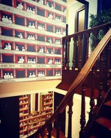Un'imponente scalinata con elaborate balaustre in legno e una ringhiera, che conduce a un piano inferiore con scaffali pieni di figurine bianche.