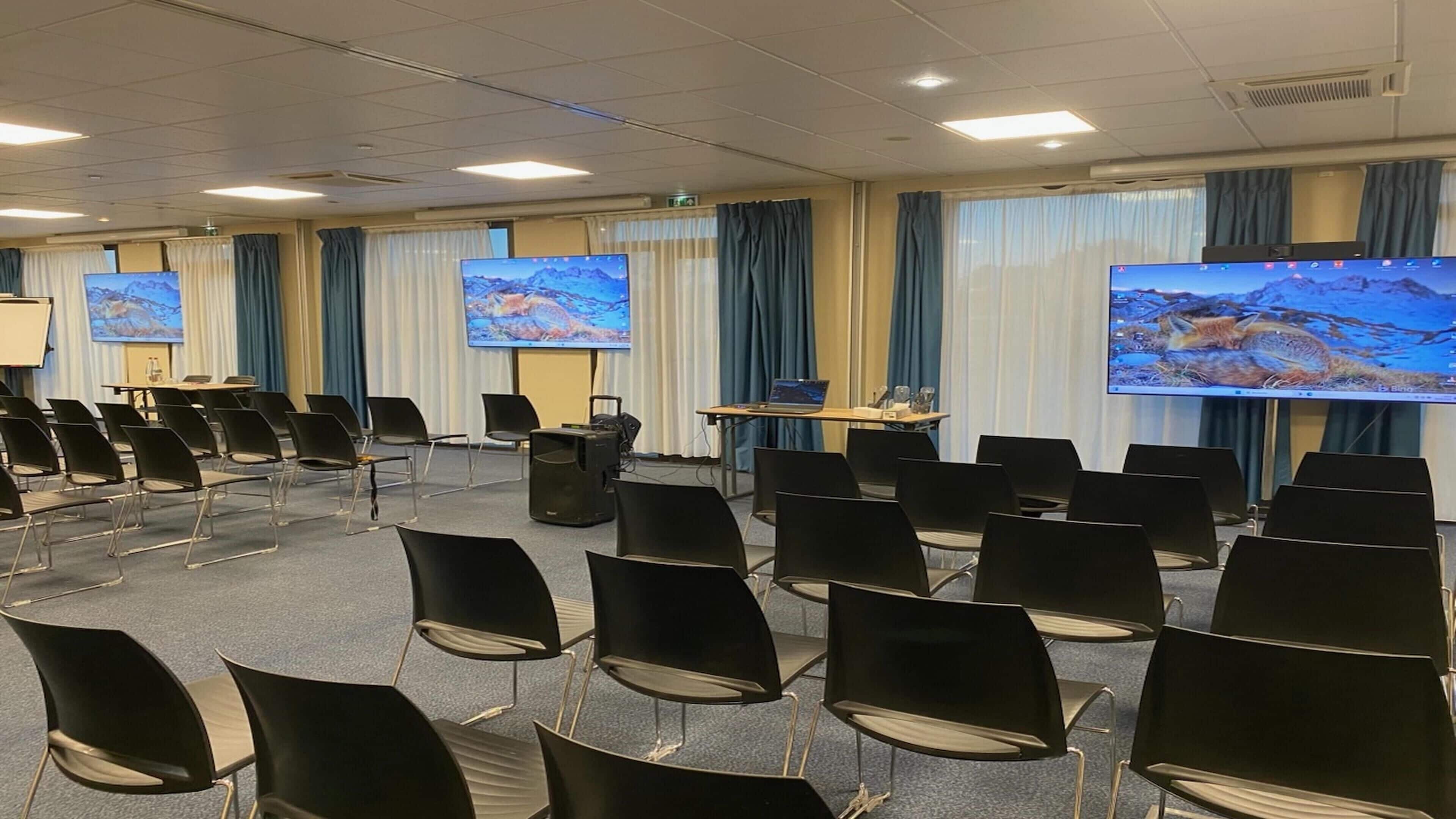 A conference room with rows of black chairs, a large screen, and a projector.