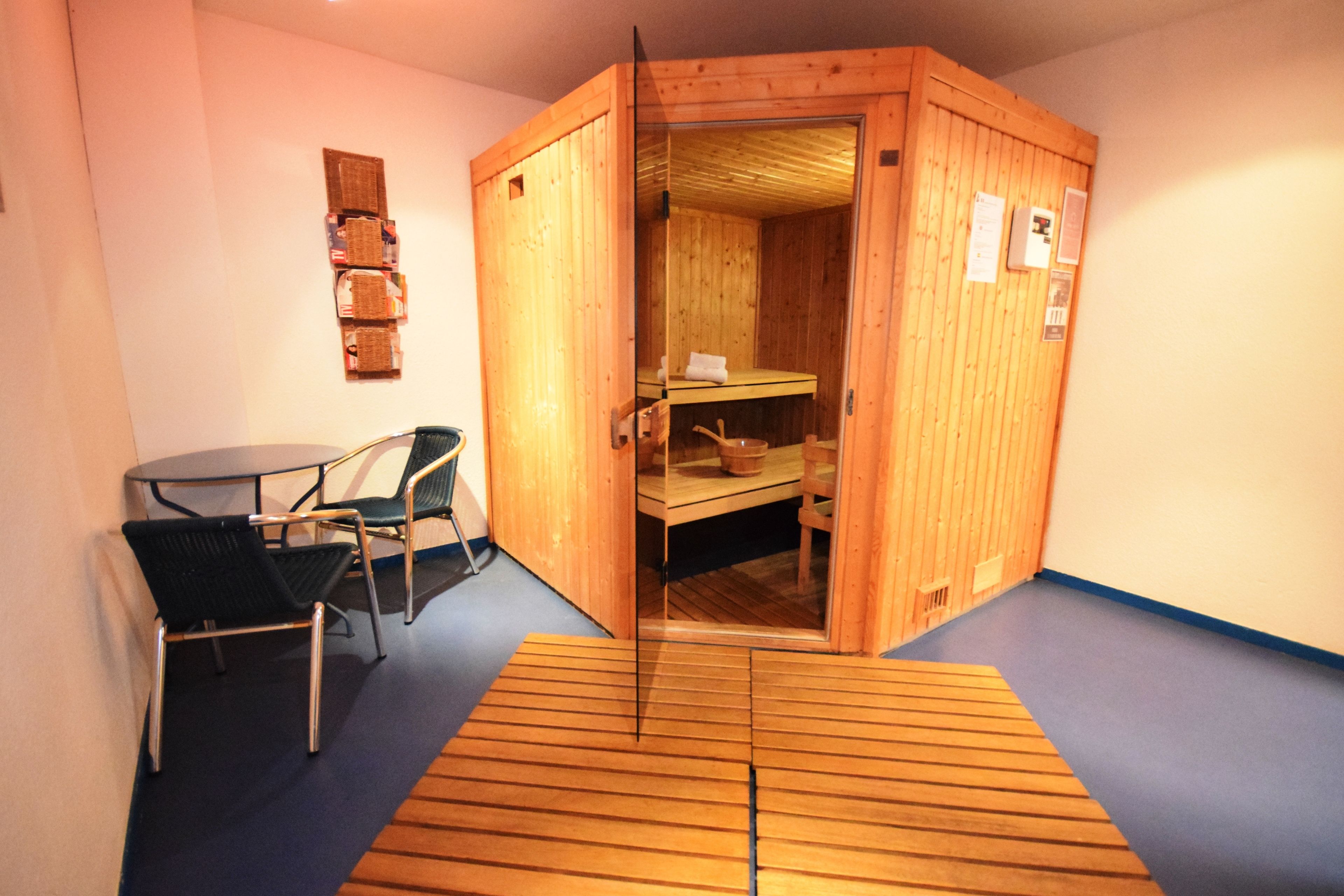 A sauna room with a wooden door, a small table with chairs, and a blue floor.