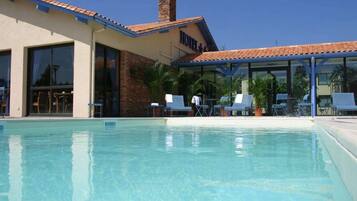 A hotel with a swimming pool, outdoor seating, and a covered patio area.