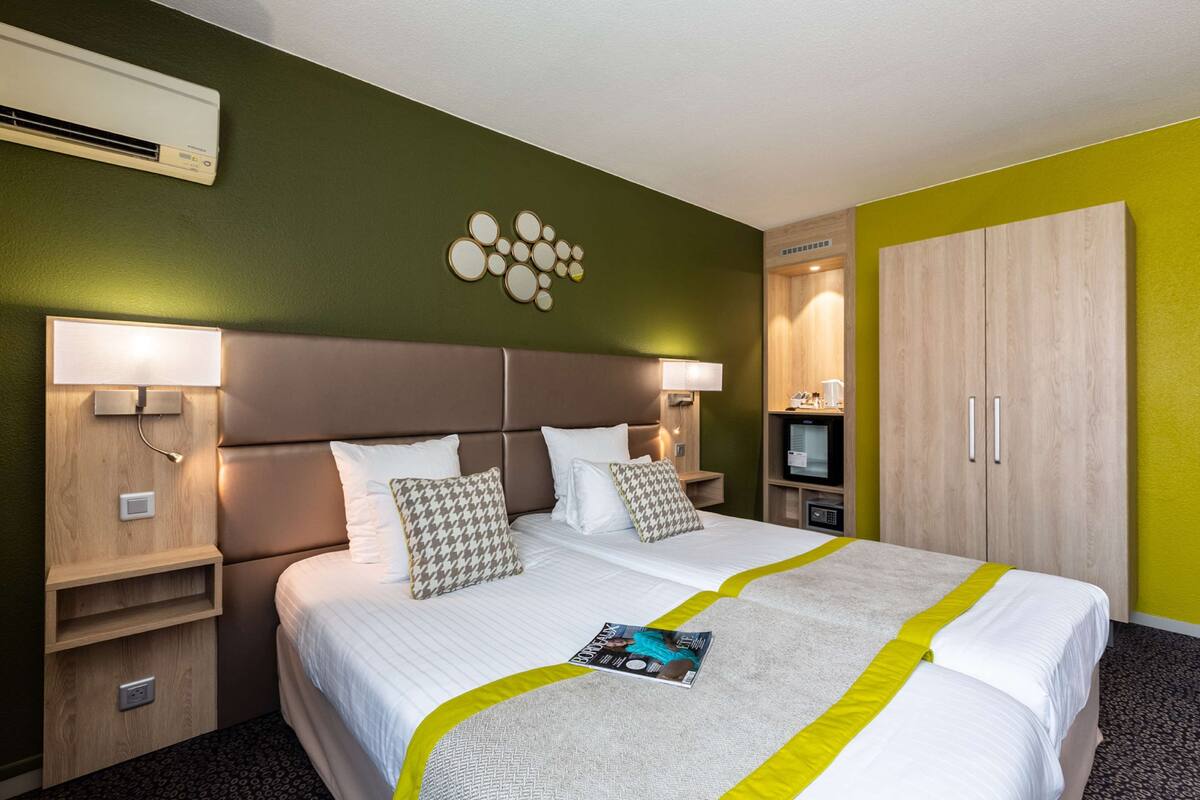 Une chambre d’hôtel avec un grand lit, deux tables de chevet avec des lampes, une armoire et un climatiseur fixé au mur.