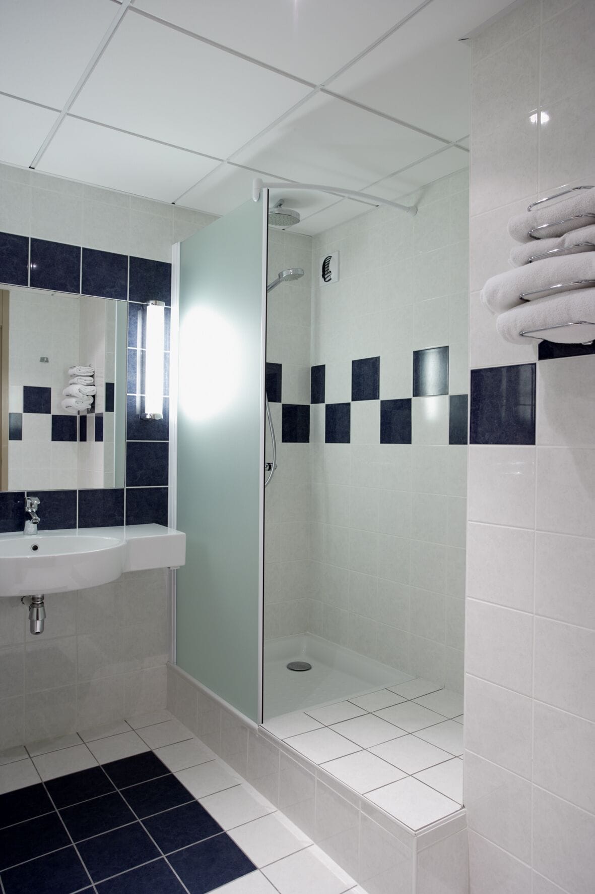 Ein modernes Badezimmer mit einer Duschkabine, einem Waschbecken mit Spiegel und Fliesenboden.