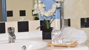 A bathroom sink with a chrome faucet, a potted orchid, and toiletries on a wooden tray.