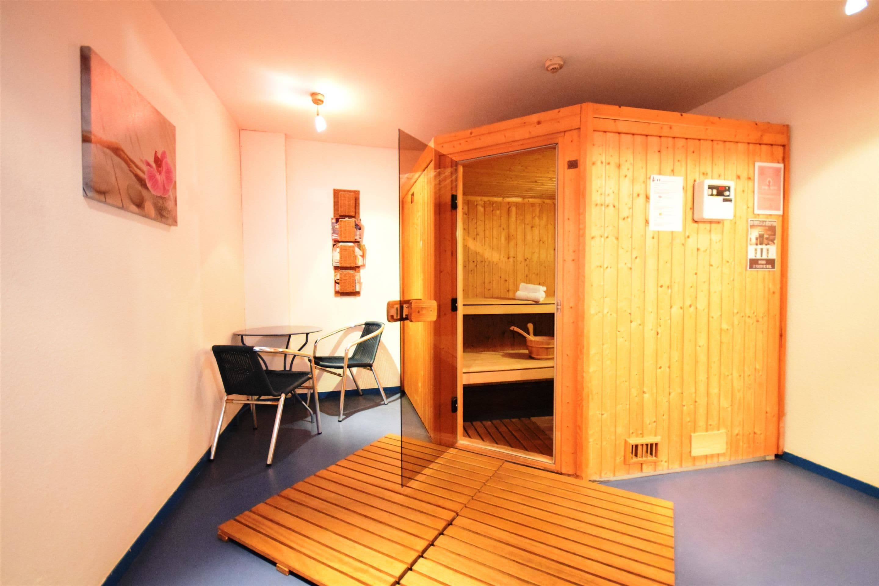 Una sala de sauna con puerta de madera, una pequeña mesa y una silla.