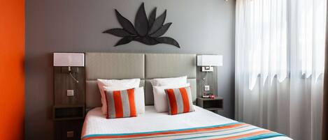 Quarto de hotel com uma cama grande, duas mesas de cabeceira, uma luminária na parede e uma janela com cortinas.