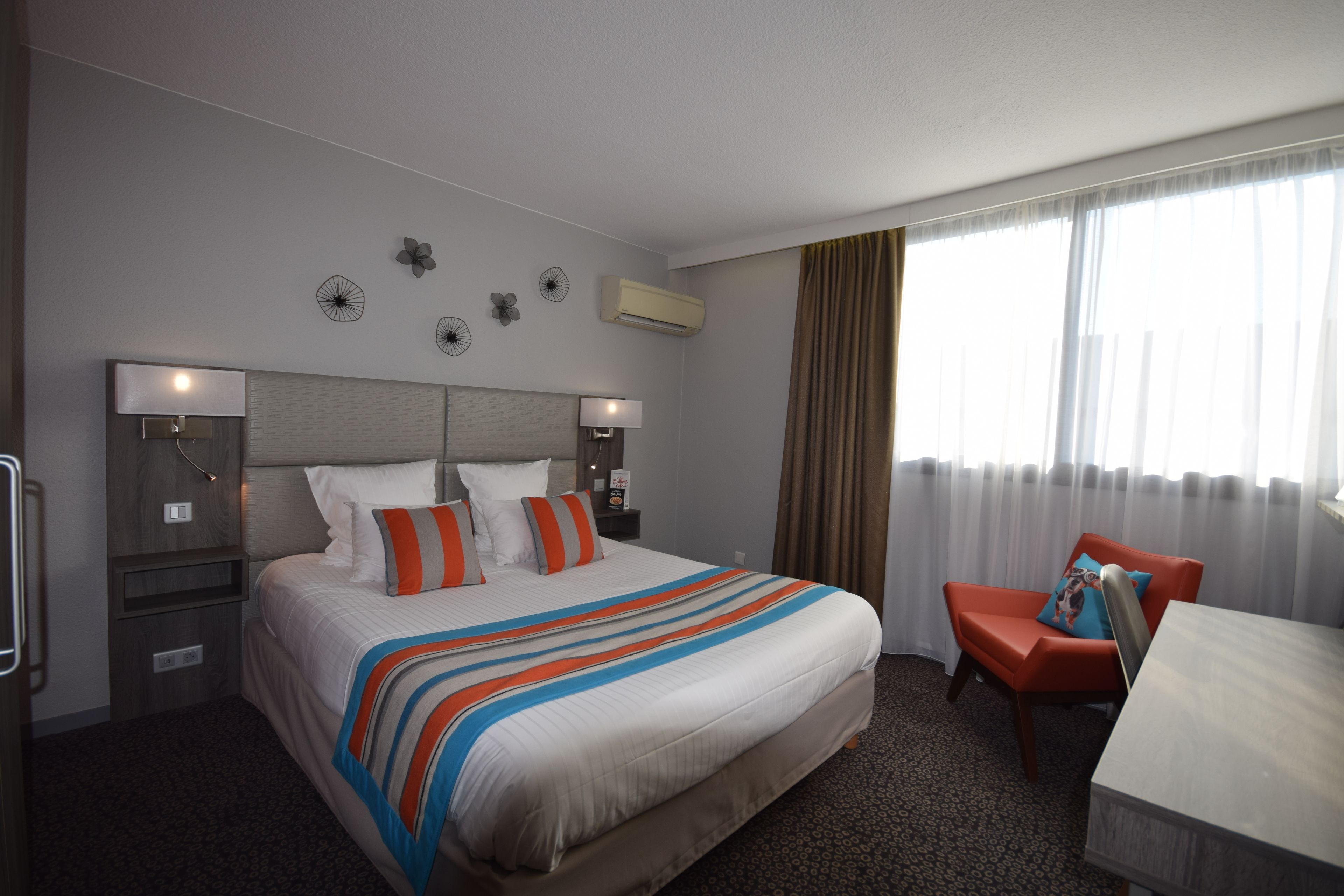 Habitación de hotel con una cama grande, dos mesitas de noche, un escritorio y una silla. Cuenta con decoraciones en las paredes y un equipo de aire acondicionado.