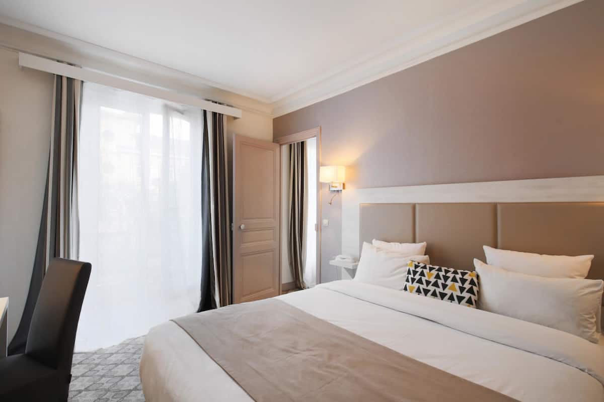 A hotel room with a large bed, a desk, and a chair.