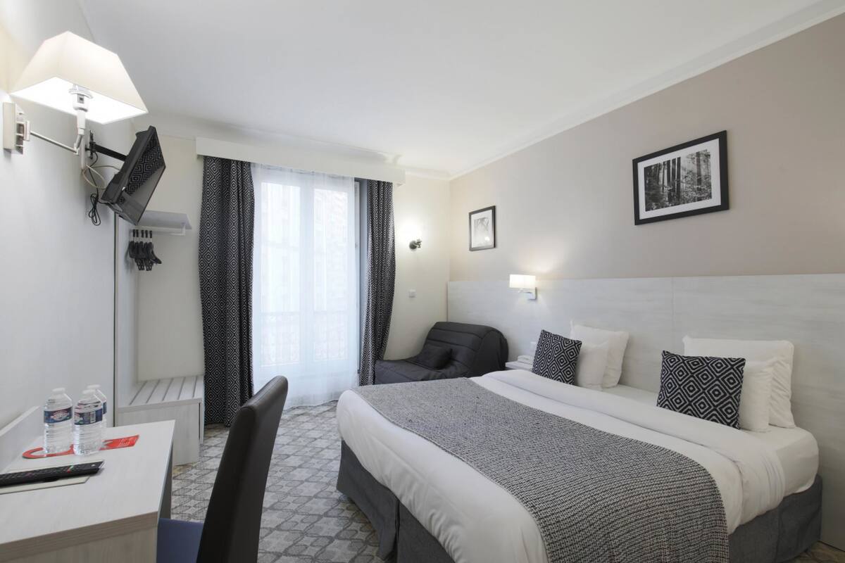 A hotel room with a bed, desk, chair, and a window with curtains.
