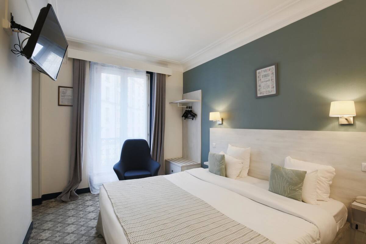 A hotel room with a large bed, a flat-screen TV mounted on the wall, a desk with a lamp, and a chair.