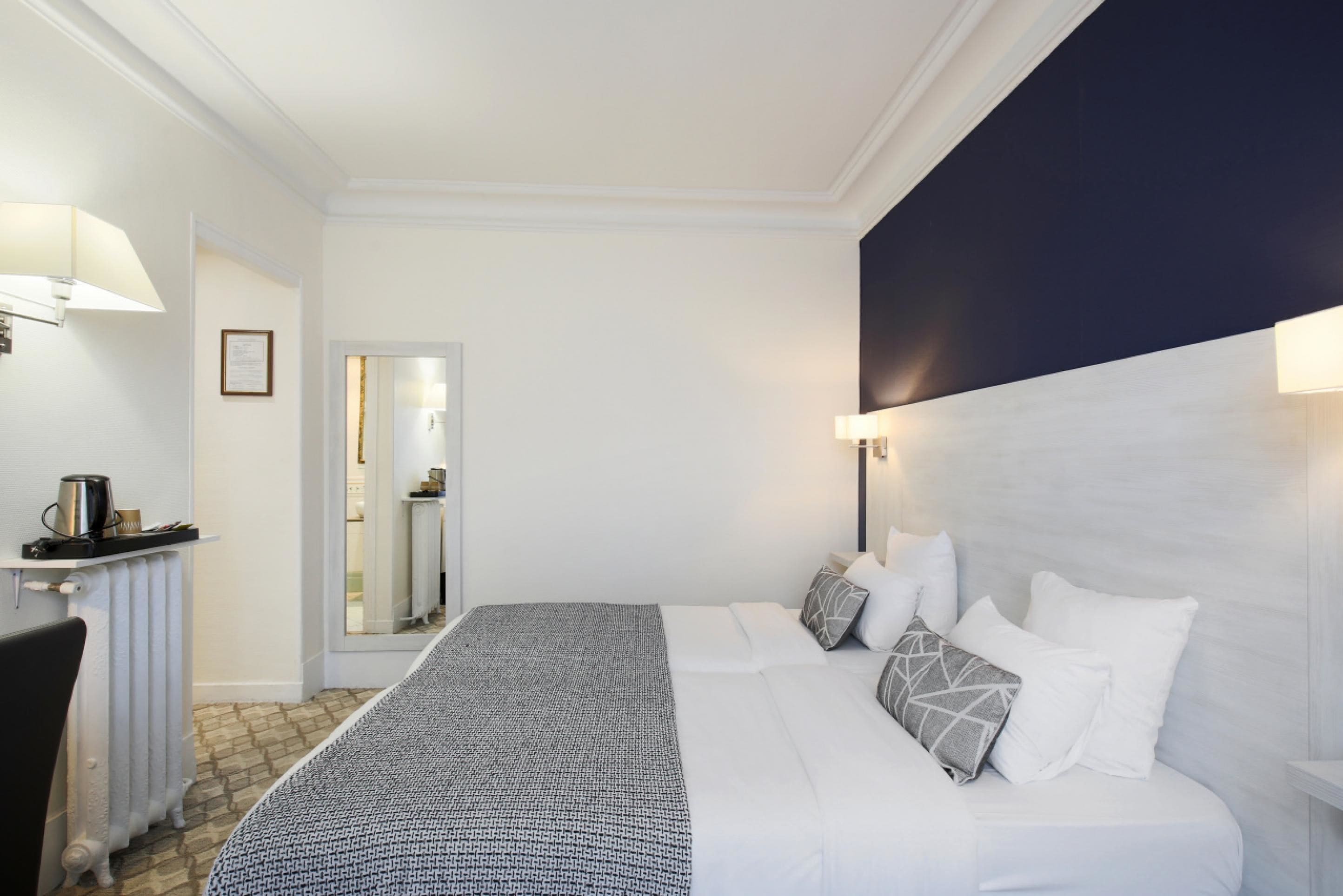 A hotel room with a neatly made bed, a bedside table with a lamp, and a view of the bathroom through an open door.