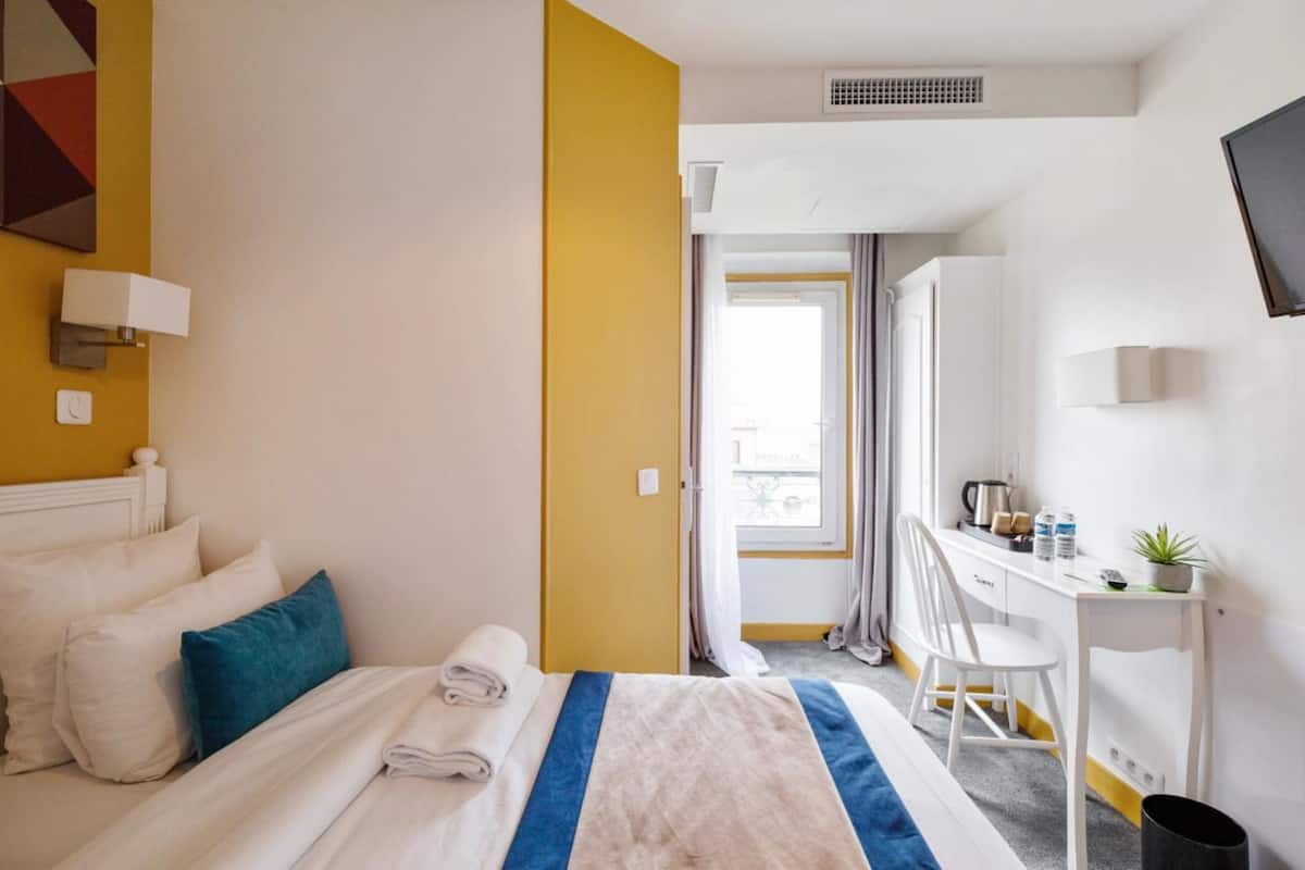 A hotel room with a bed, a desk, a chair, a TV, and a window.