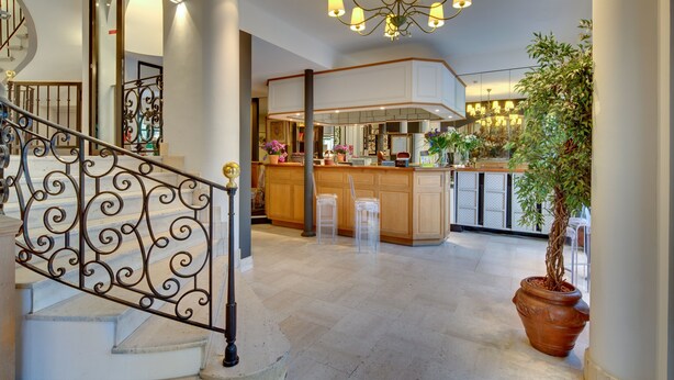 A spacious kitchen with a central island, a staircase with ornate railings, and a large potted plant. - Grand Hotel des Gobelins (Paris)