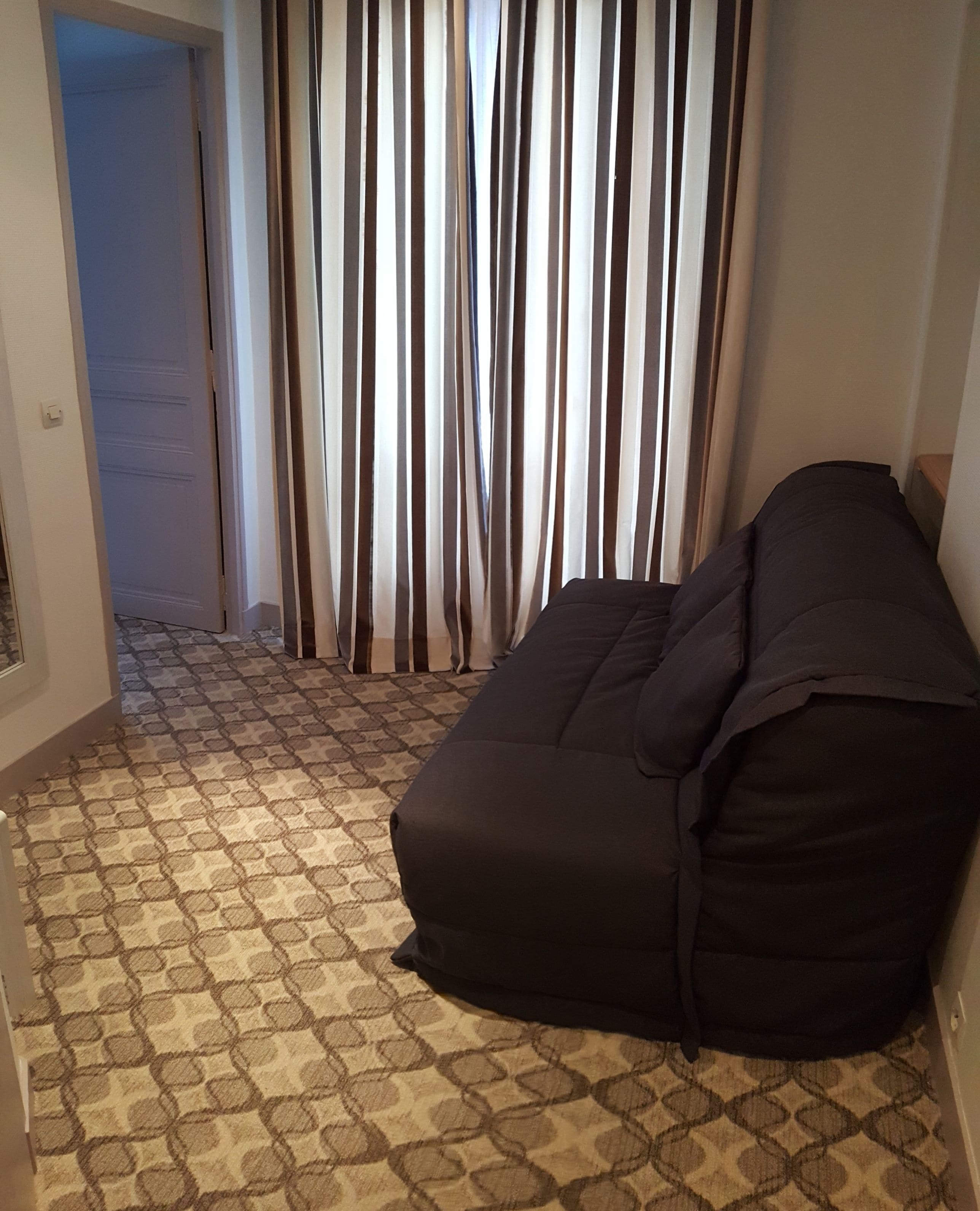 A room with a patterned carpet, a black sofa, and a curtain with vertical stripes.