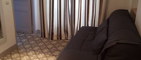 A room with a patterned carpet, a black sofa, and a curtain with vertical stripes.