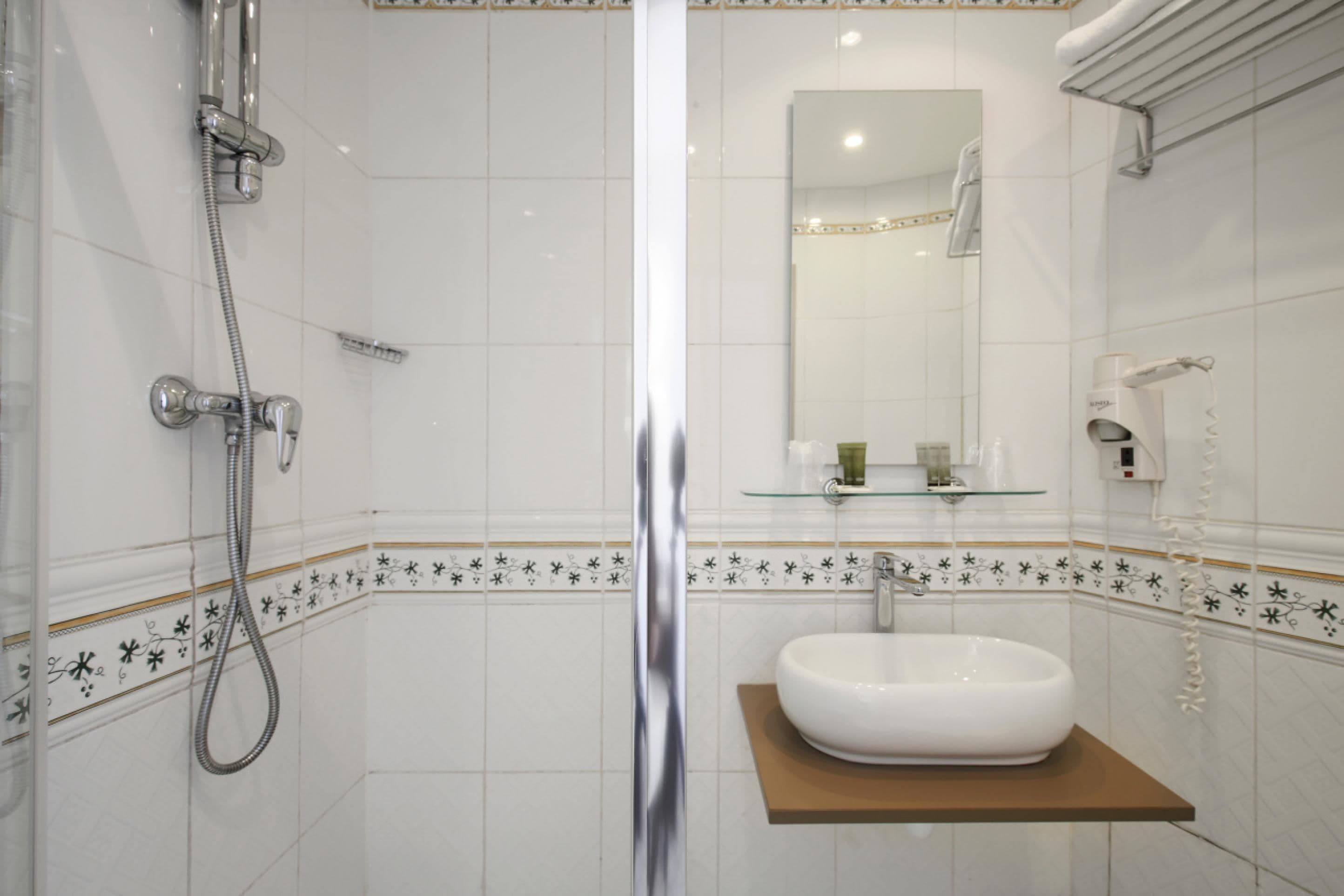 Un baño con ducha de vidrio, un lavabo blanco sobre un estante de madera y un espejo sobre el lavabo.