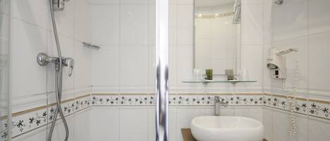 Un baño con ducha de vidrio, un lavabo blanco sobre un estante de madera y un espejo sobre el lavabo.