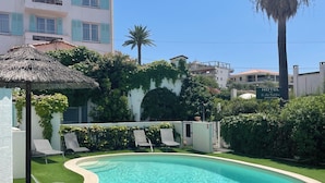 A swimming pool with lounge chairs, a thatched umbrella, and a building with a sign reading "HOTEL". - Hôtel Le Pré Catelan (Antibes)