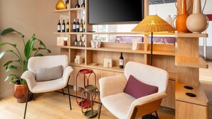 Ein modernes Interieur mit zwei Sesseln, einem Fernseher, Weinflaschen und einem Blumentopf.
