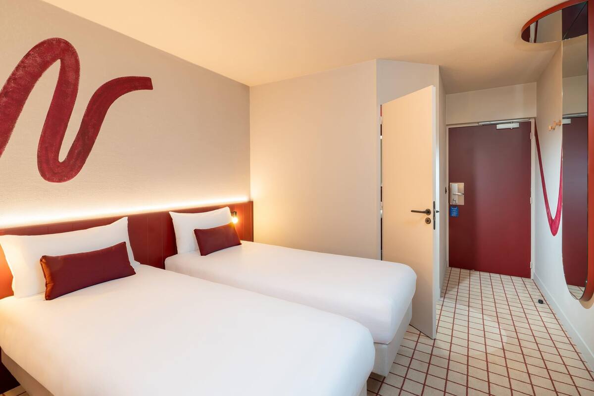 Ein Hotelzimmer mit zwei Betten, einem großen Spiegel und einer Tür zu einem anderen Raum.
