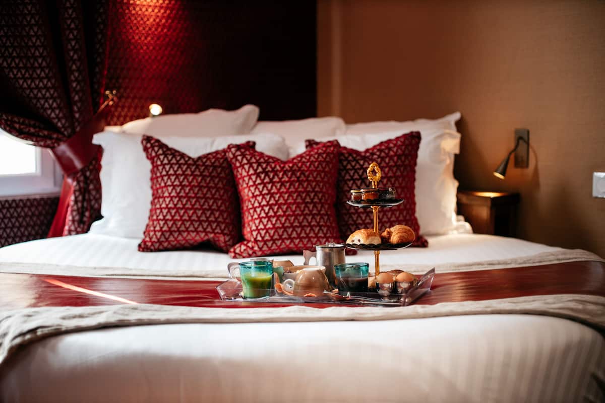 Un lit bien fait, agrémenté d’oreillers à motifs rouges, un plateau avec des articles pour le petit-déjeuner et une lampe de chevet.