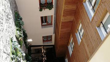 A narrow alleyway between buildings with wooden facades, multiple windows, and hanging plants.