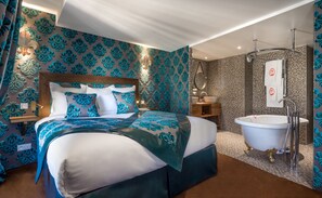 A modern bedroom with a large bed, a vanity with a mirror, and a bathtub. - Hôtel Le Temple de Jeanne (Paris)