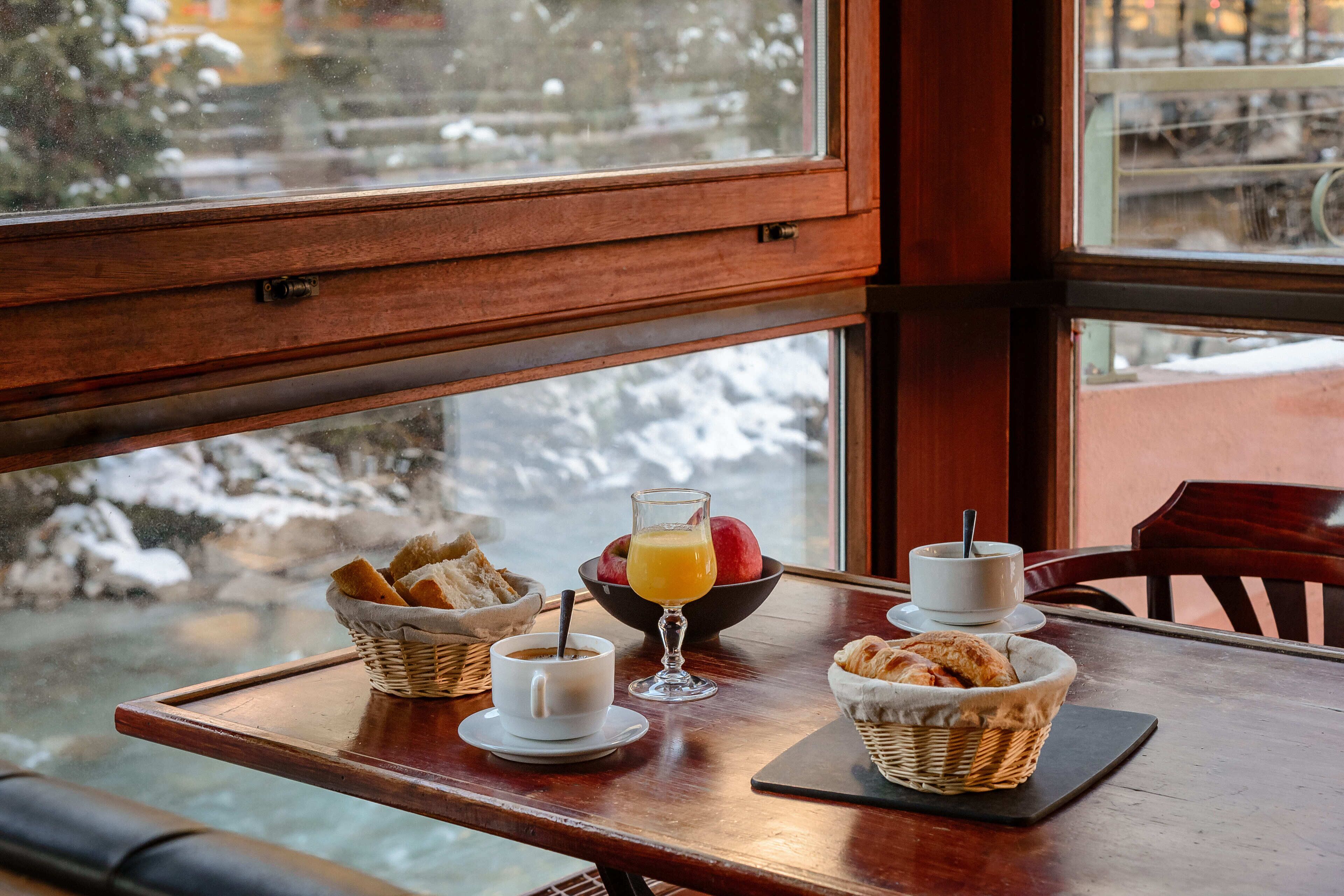A breakfast table with a basket of bread, a bowl of fruit, a glass of orange juice, and a cup of coffee.