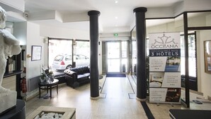 A hotel lobby with a reception desk, a sofa, and a large poster advertising three hotels. - Occitania Centre Toulouse Matabiau (Toulouse)