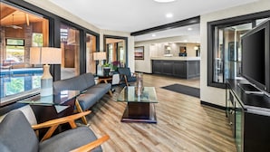 A modern living room with a sofa set, a glass coffee table, and a television. There is a kitchen area in the background with a countertop and cabinets.