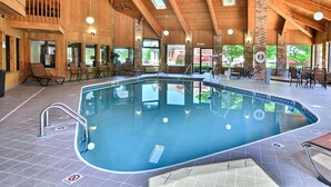 A large indoor swimming pool with a wooden interior, multiple seating areas, and large windows.