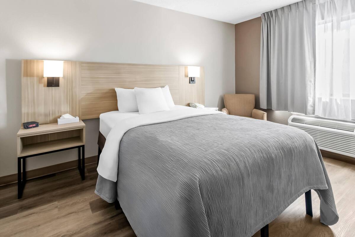 A hotel room with a large bed, bedside tables, a chair, and a window with curtains.