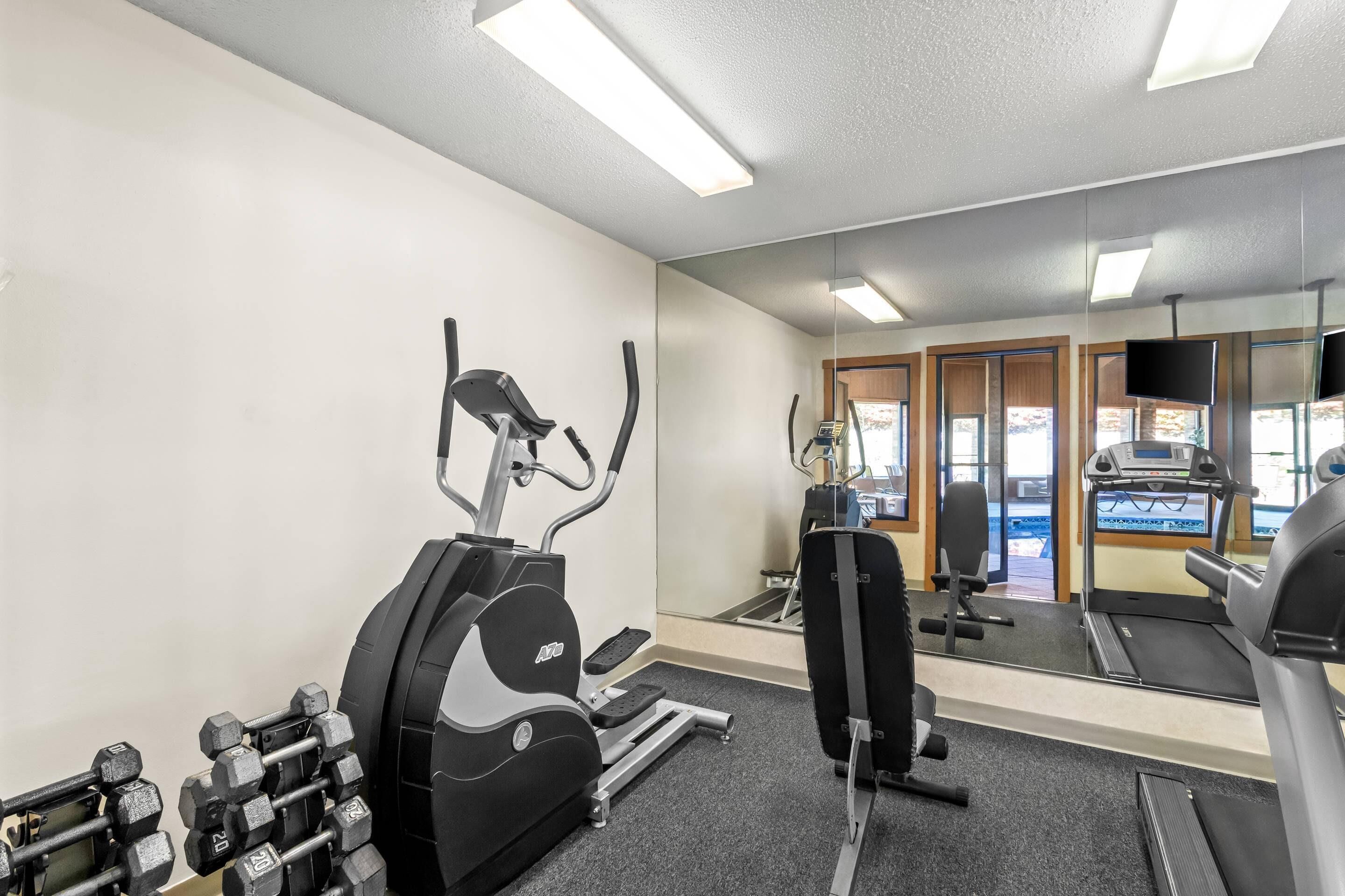 A gym with cardio machines, dumbbells, and a mirrored wall.