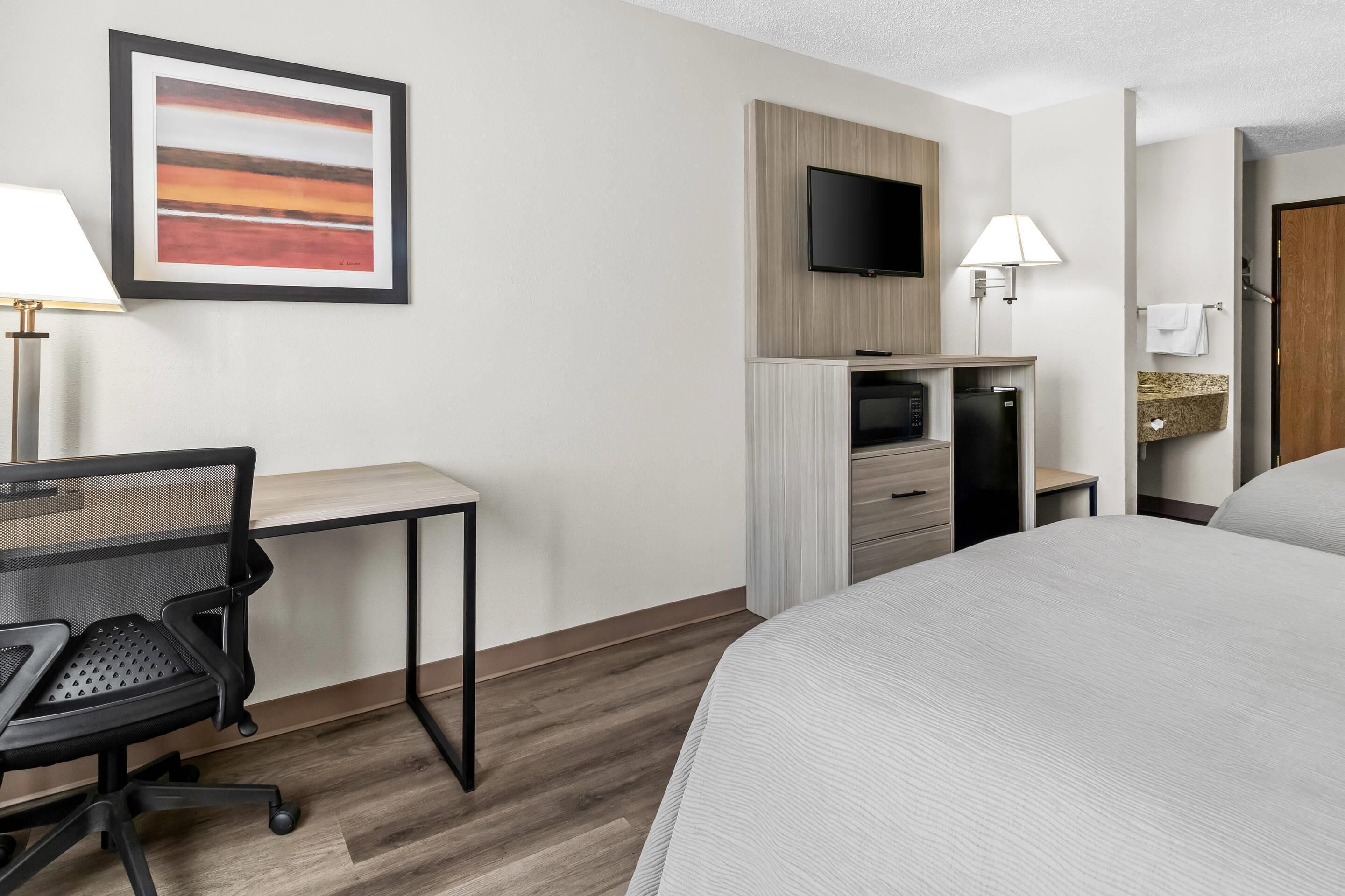 A hotel room with a bed, desk, chair, TV, and a framed picture on the wall.