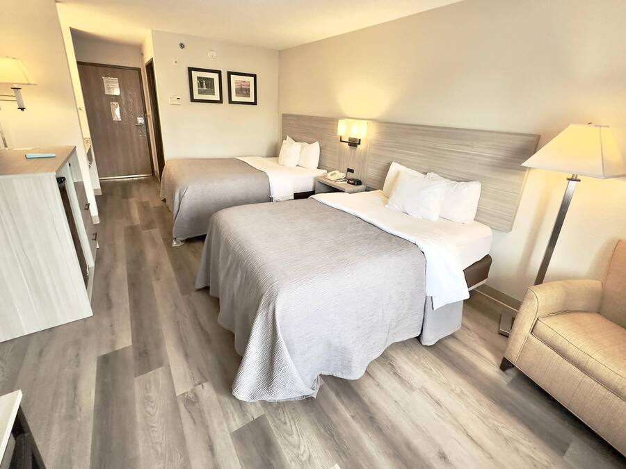 A hotel room with two beds, a desk, a chair, and a TV.