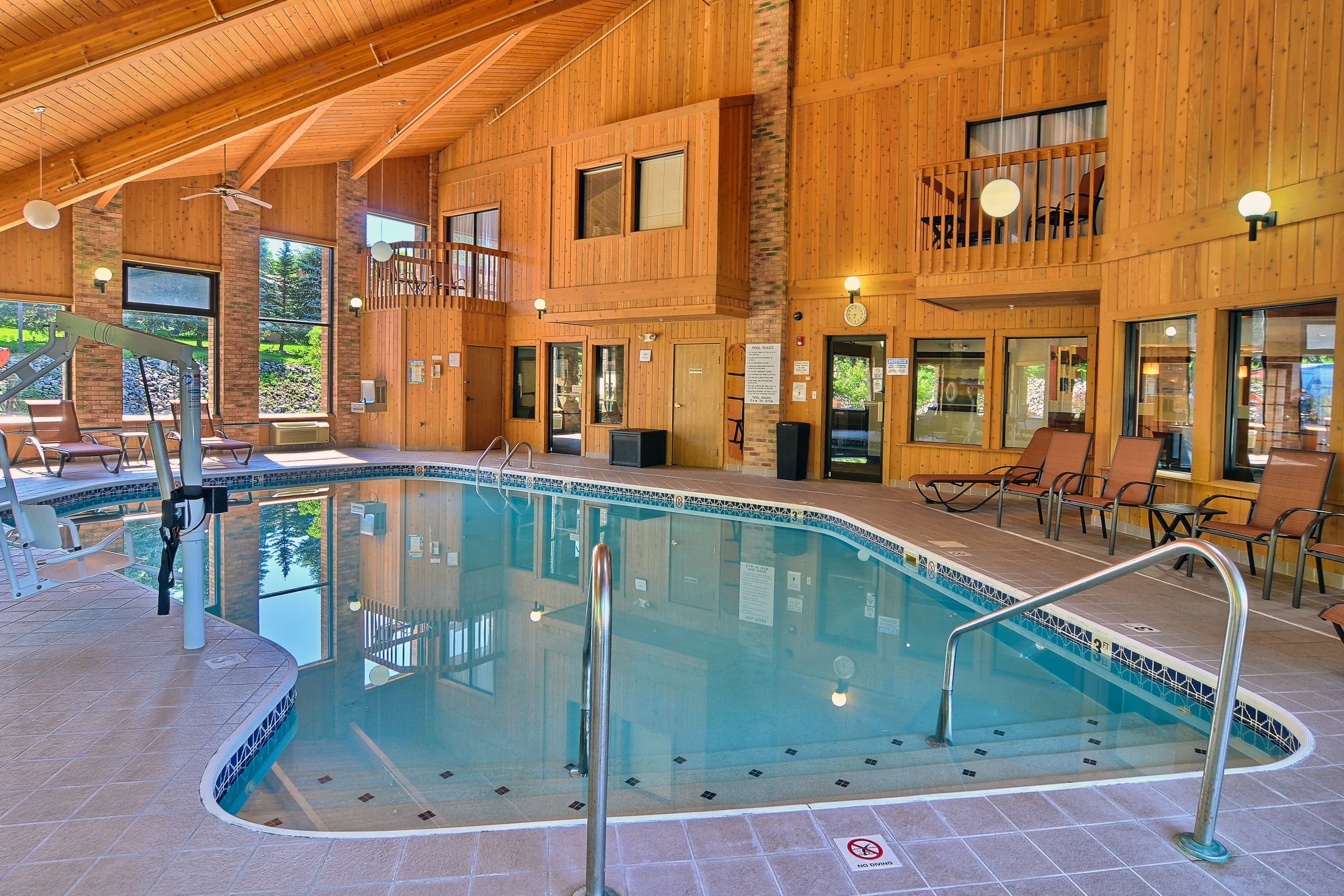 An indoor swimming pool with a wooden interior, multiple windows, and a balcony.