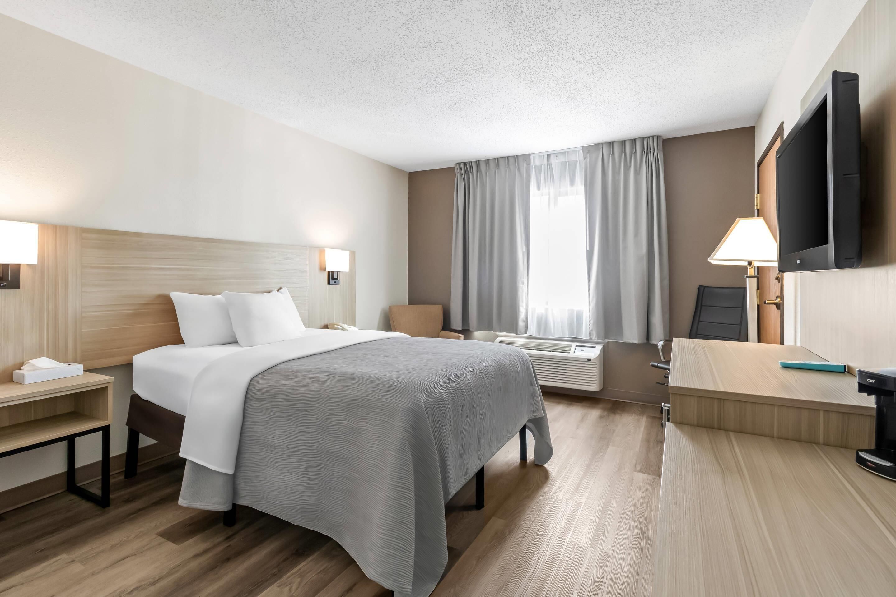 A hotel room with a bed, bedside tables, a desk, a flat-screen TV, and a window with curtains.
